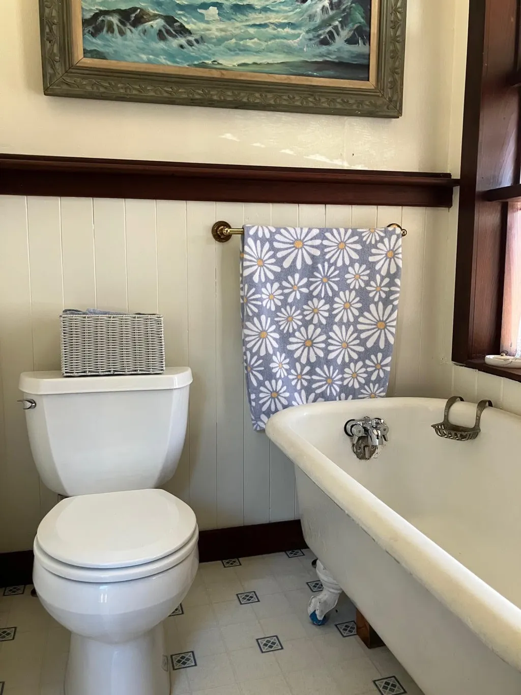 A cast-iron clawfoot tub and white beadboard beneath a painting of the surf