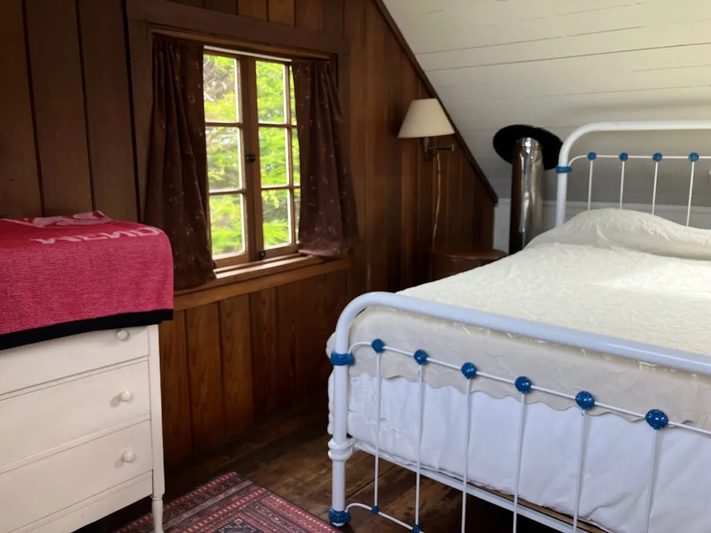 The second upstairs bedroom with a white iron bed, redwood walls, and a sloped whitewashed ceiling