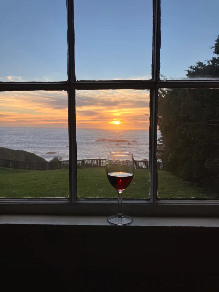 A glass of wine on the sill as the sun sets over the water